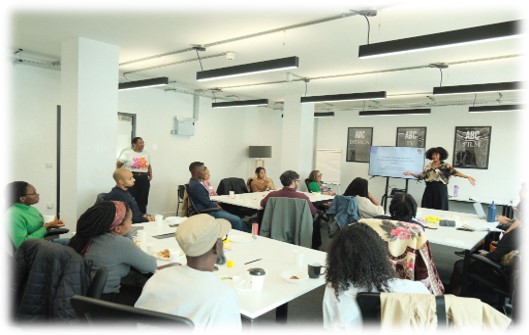 People sitting at tables in a room with Yolanda presenting at the front.